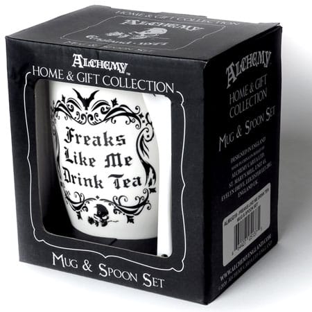 Boxed gift that includes a mug and spoon set. It is white and printed with a high contrast black design that reads: "Freaks Like Me Drink Tea" with bordering scrolls and accented with a bat. The spoon bears a skull holding a rose in the mouth printed on the bowl of the spoon.
