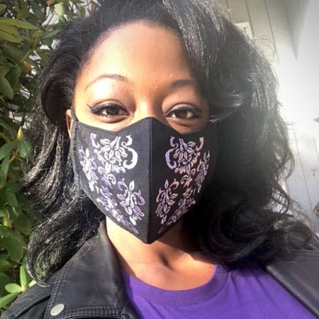 Model Yani from Massachusetts wearing a purple embroidered cotton face mask. The base of the mask is cotton and is black in color.