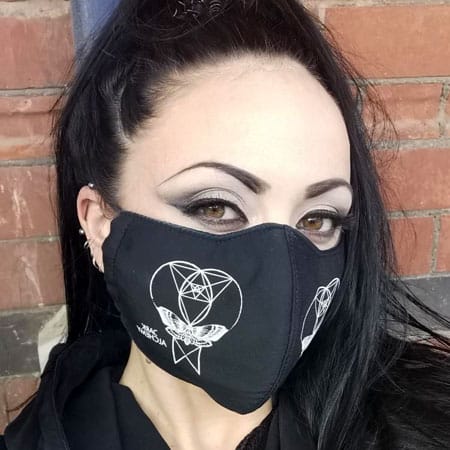 Miss Fortune London wearing a 3 layer black cotton face mask with white printing on it. The design includes sacred geometry as well as a butterfly / death moth.