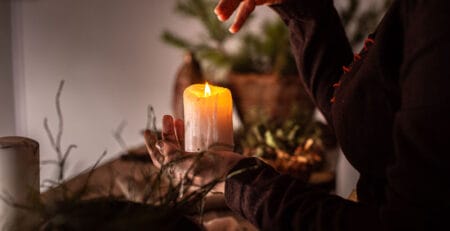 A lit candle held by a woman waving her hand over it.